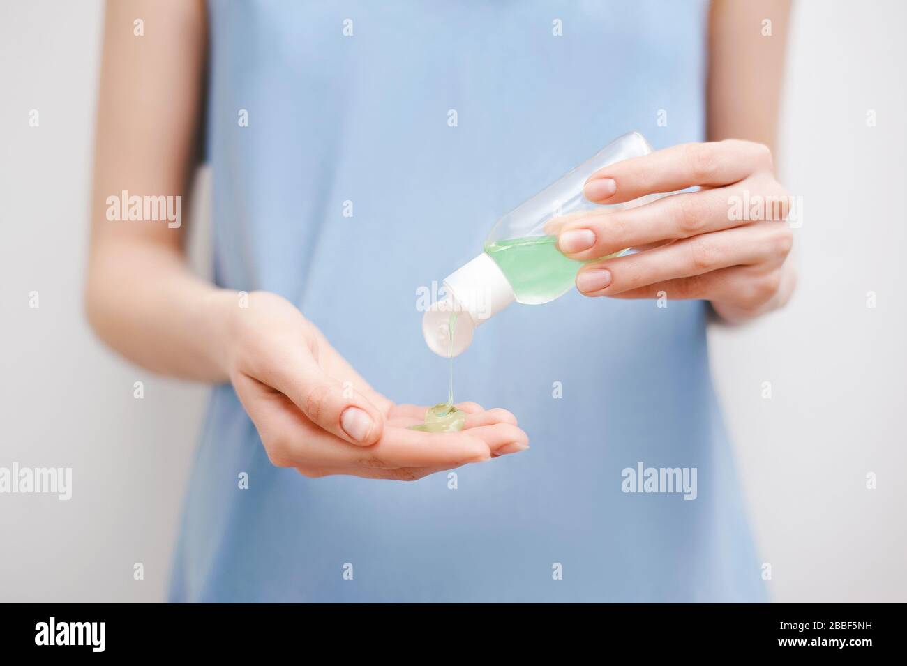 Vista ravvicinata delle mani della donna utilizzando un antisettico o un igienizzatore personale. Misure di protezione Covid-19. Donna in abito blu su sfondo bianco pulito. Foto Stock