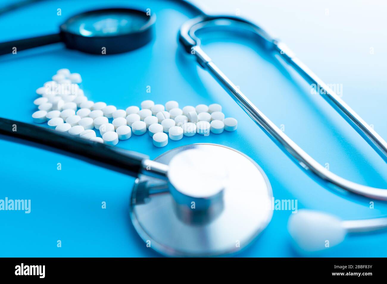 Capsule con riflesso e stetoscopio su fondo blu. Concetto di assistenza sanitaria. Messa a fuoco morbida. Foto Stock