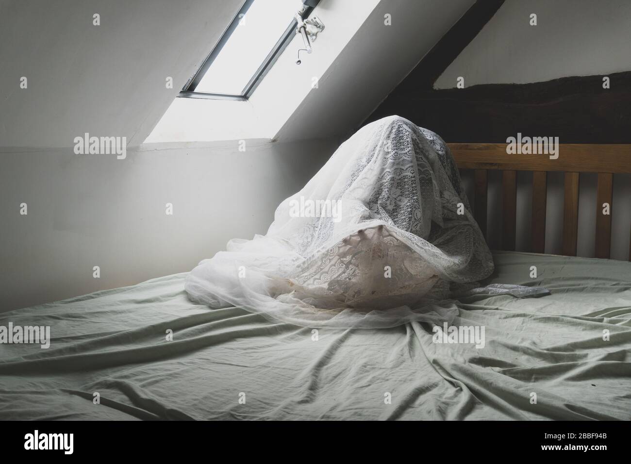 Una figura spettrale e spettrale seduta su un letto, con una mano che arriva Foto Stock