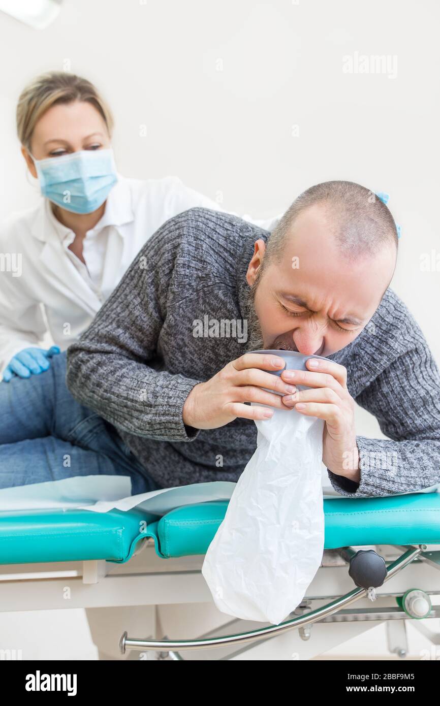 il medico o l'infermiere di sesso femminile sta osservando un paziente maschio mentre vomita, il concetto del virus corona o covid-19, sars-cov-2 Foto Stock