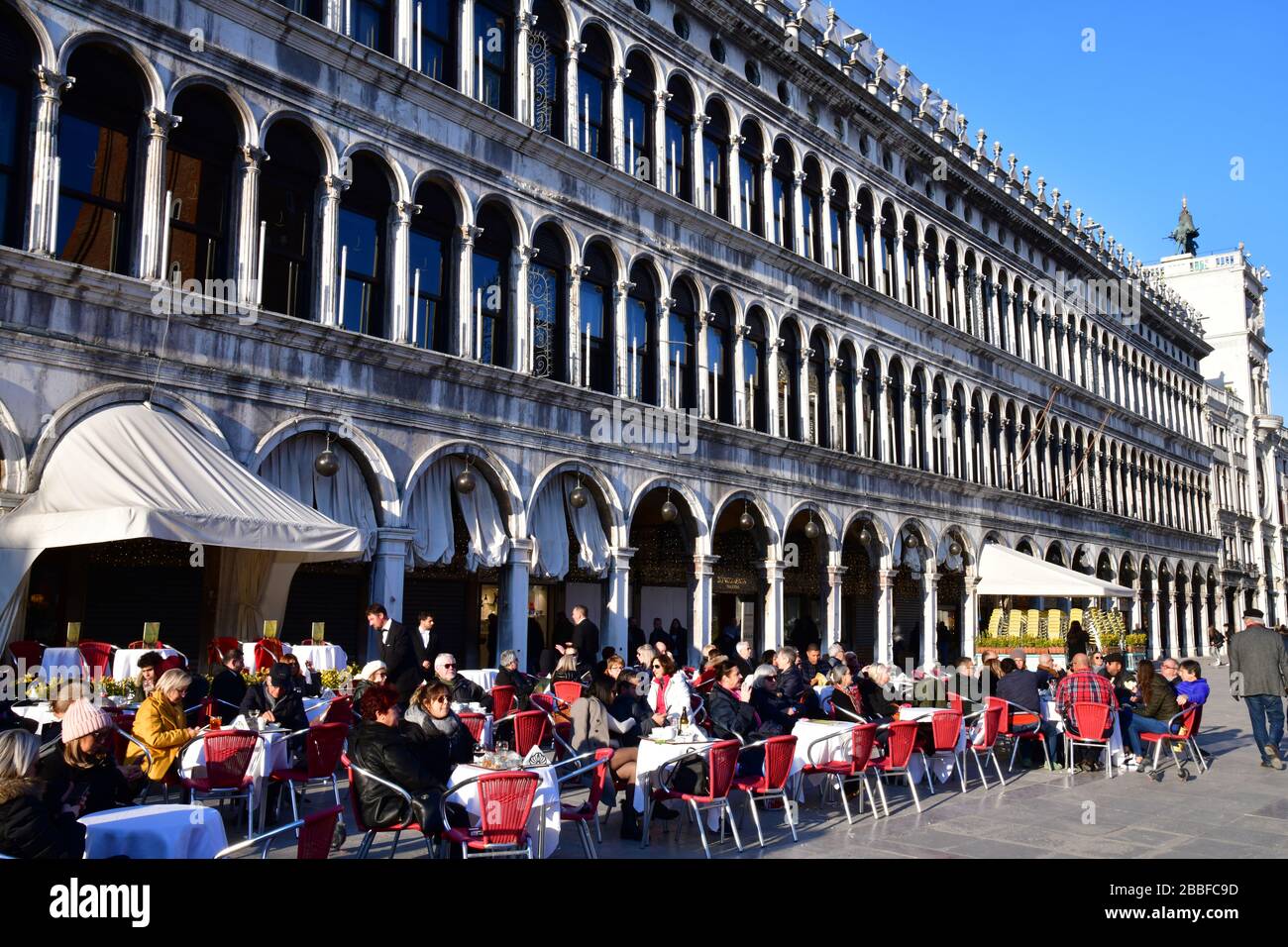 Vista laterale su una delle terrazze che costeggiano Piazza San Marco, piena di gente che cattura il piccolo calore del sole d'inverno Foto Stock