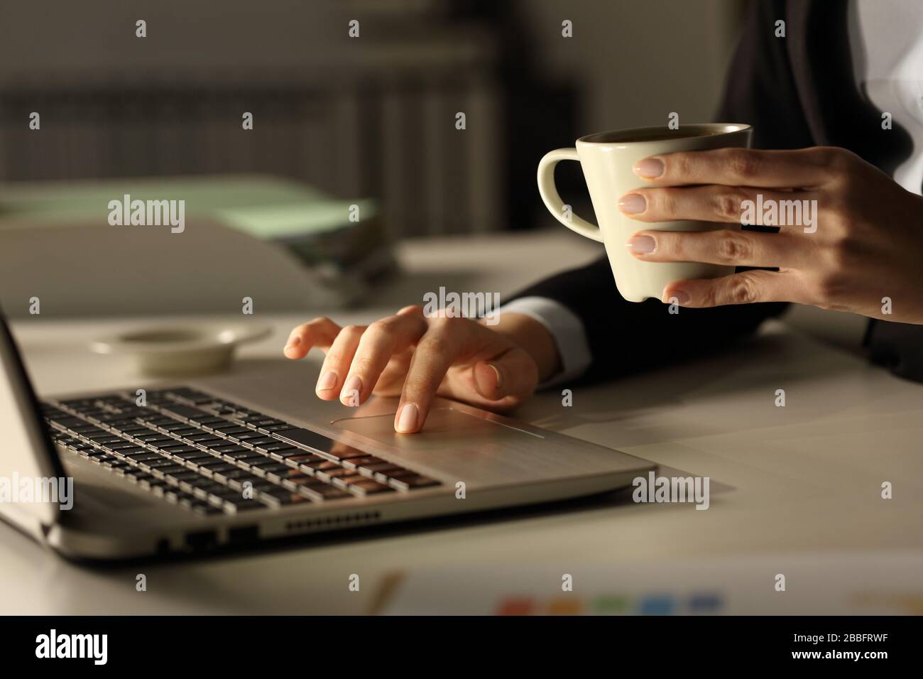 Primo piano delle mani delle donne in viaggio d'affari con il laptop che tiene la tazza del caffè di notte in ufficio Foto Stock