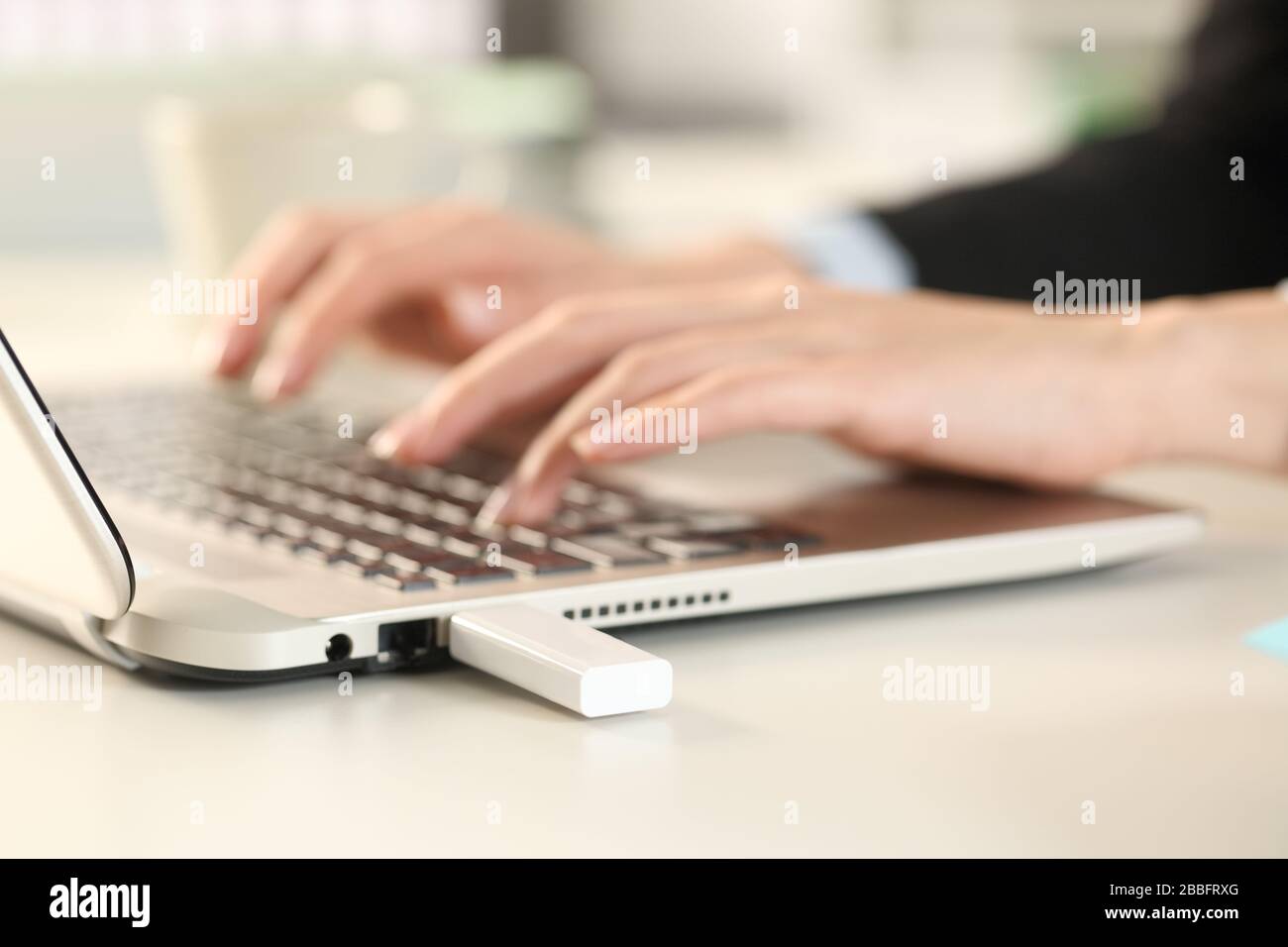 Primo piano delle mani di una donna executive utilizzando un computer portatile con un pendrive collegato seduto su una scrivania in ufficio Foto Stock