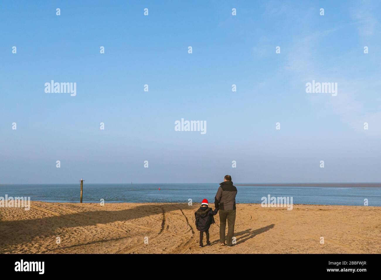Padre e figlio caucasici tengono le mani e camminano sulla spiaggia in inverno Foto Stock