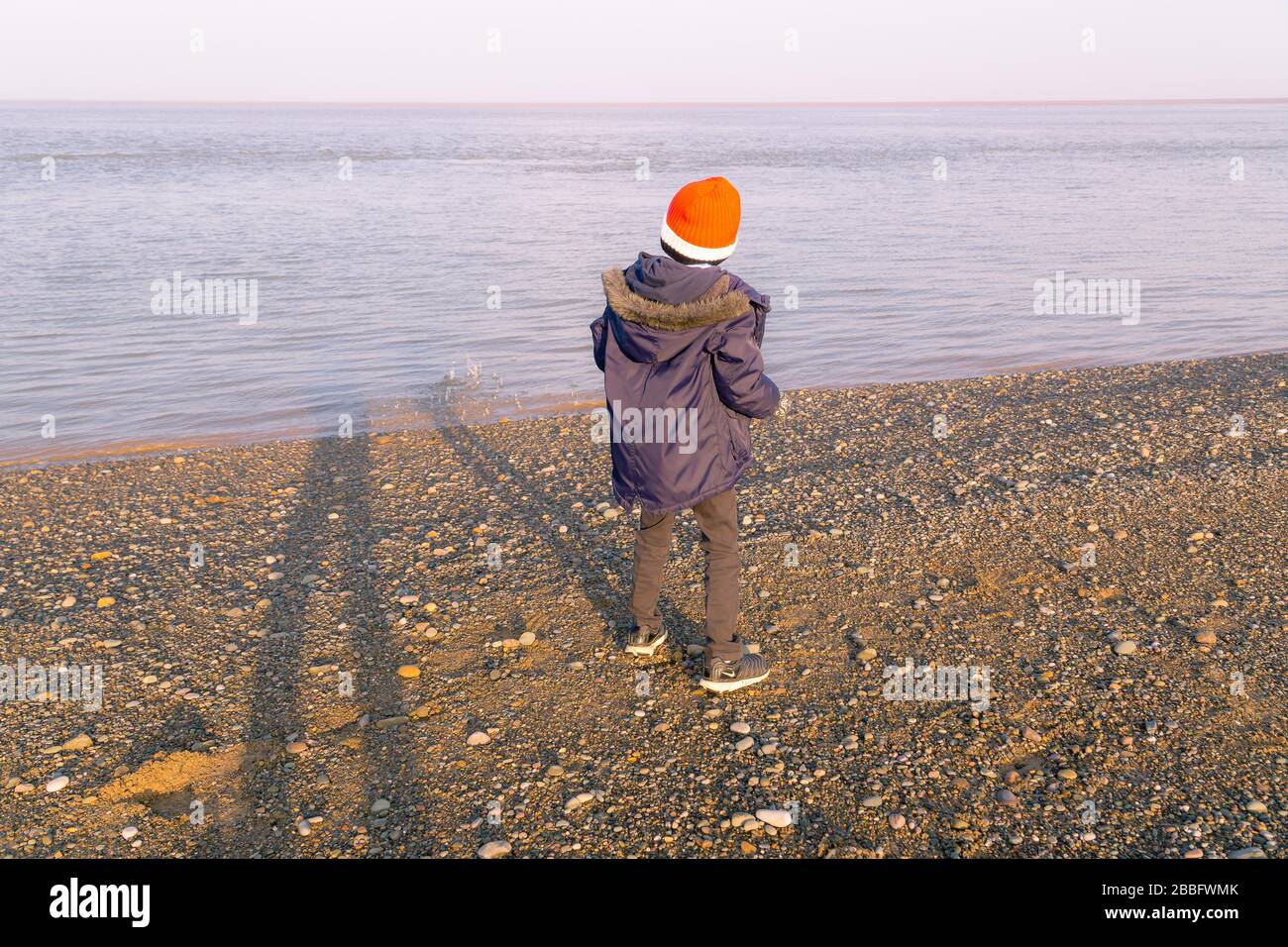Ragazzo che gettava pietre nel mare dalla spiaggia Foto Stock