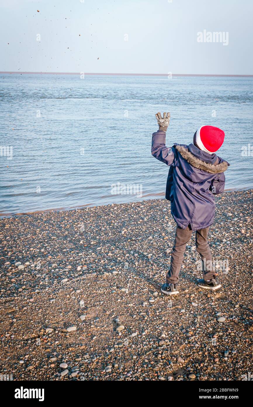 Ragazzo che gettava pietre nel mare dalla spiaggia Foto Stock