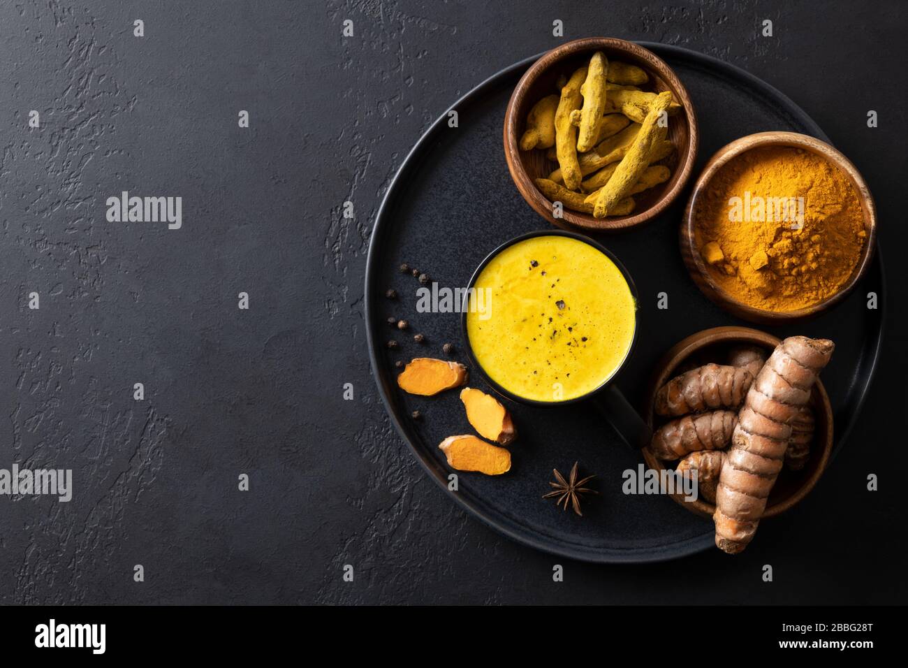 Latte d'oro con polvere di curcuma e curcuma fresca su nero. Vista dall'alto. Bevanda sana per migliorare l'immunità. Spazio di copia. Foto Stock