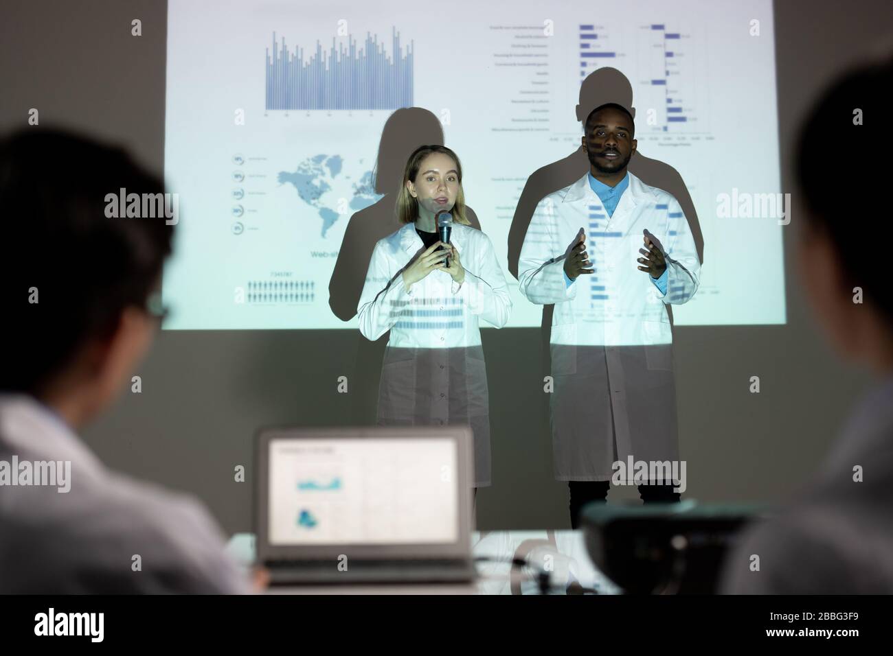 Inverni multietnici fiduciosi in camici da laboratorio che presentano il progetto scientifico davanti alla commissione in occasione di una conferenza Foto Stock