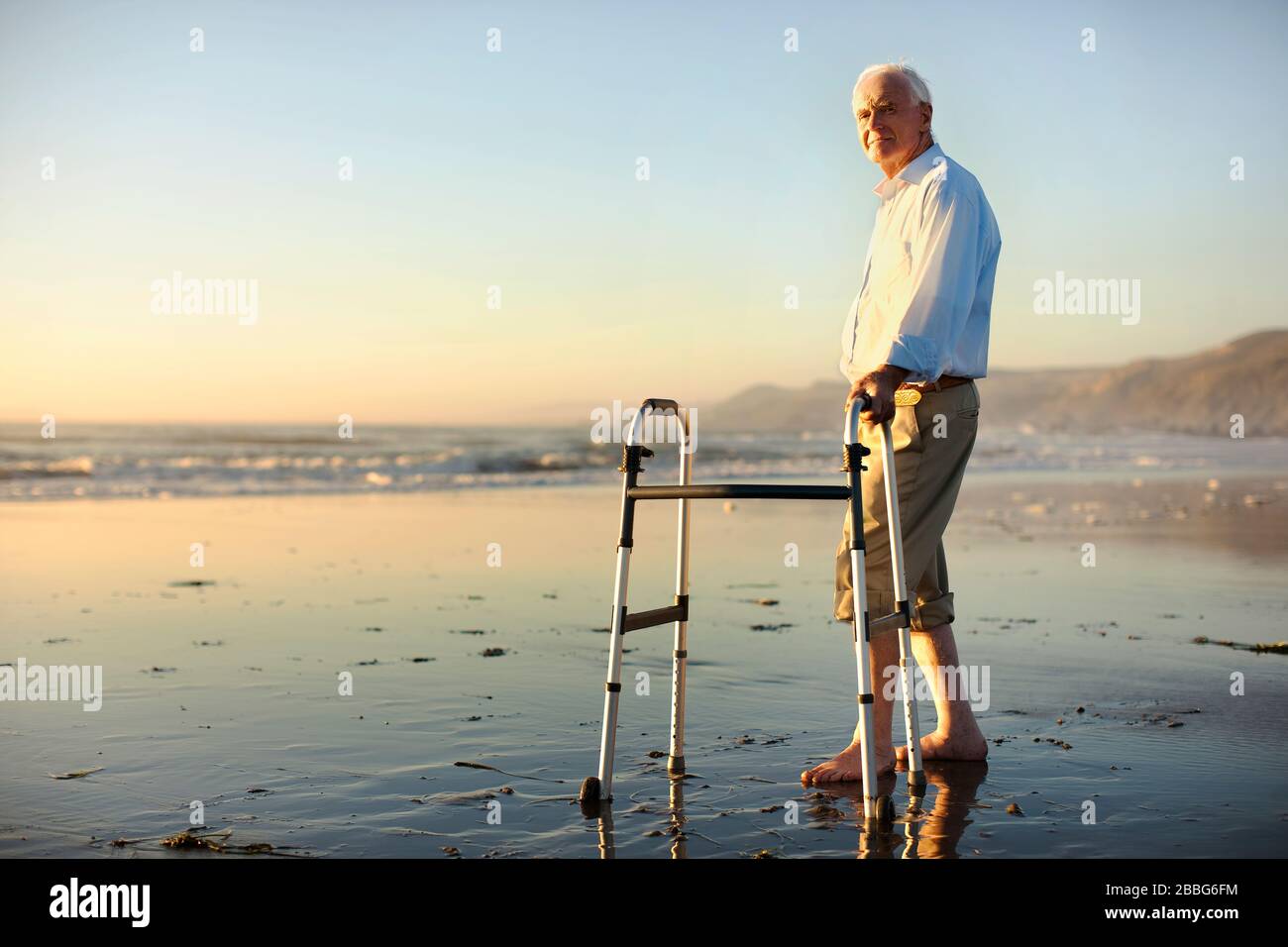 Ritratto di un anziano uomo in piedi su una spiaggia con un aiuto a piedi. Foto Stock