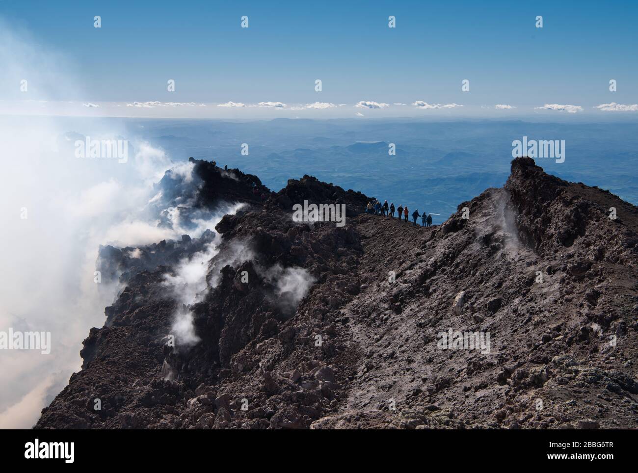 Il vapore acqueo e altri gas vulcanici traboccano dai crateri sommitali dell'Etna, versando sulle pendici superiori del vulcano. La gente sta scomparendo nel vapore. Foto Stock