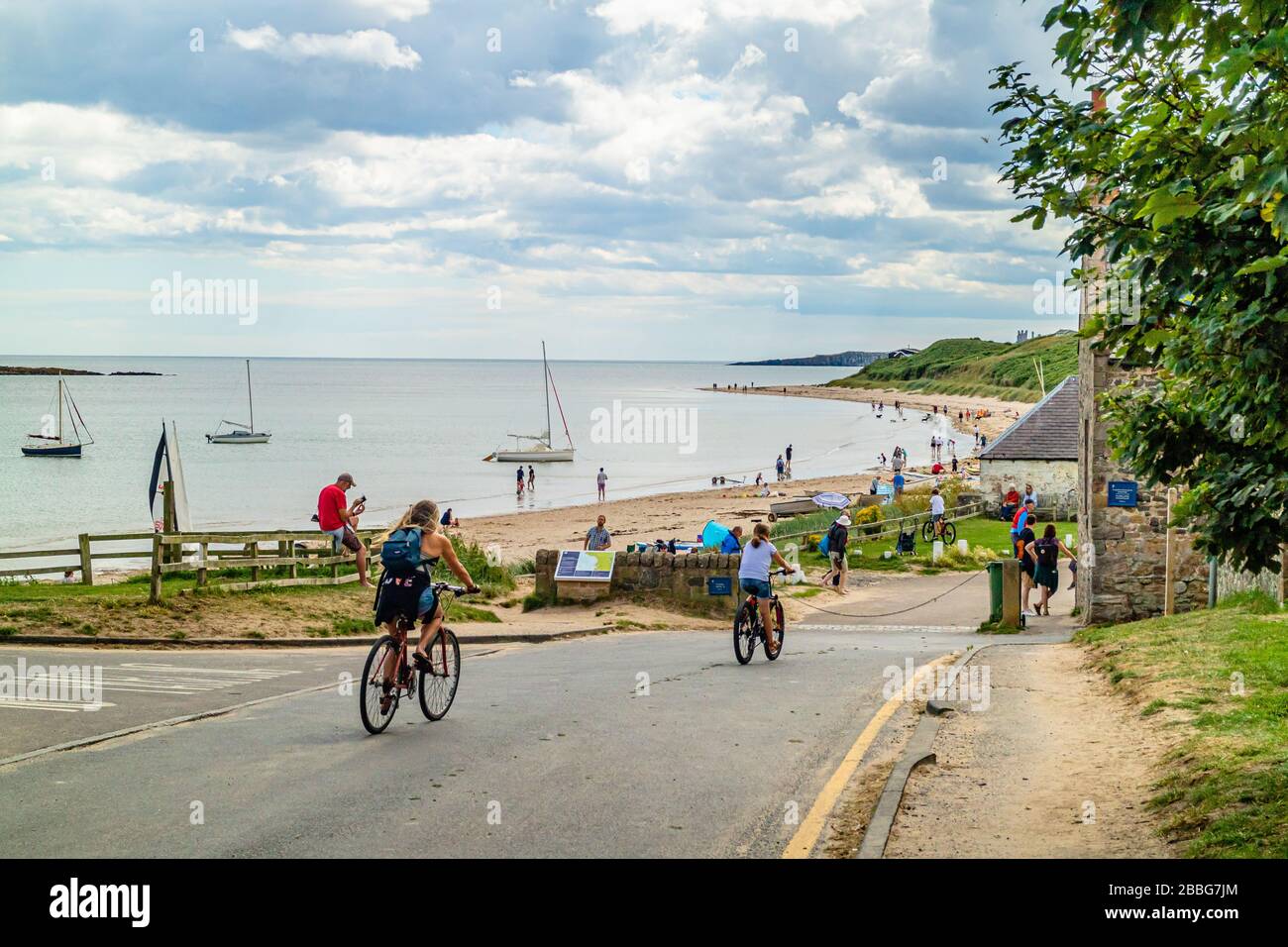 Ciclisti che passano la spiaggia di Low Newton-by-the-Sea in una giornata estiva intensa. Northumberland, Regno Unito. Agosto 2018. Foto Stock