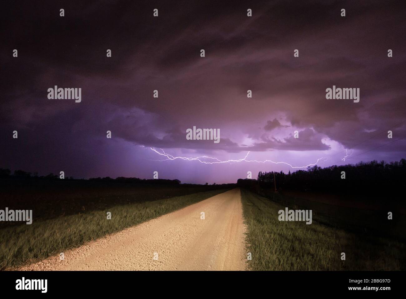 Tempesta con fulmini lampeggiante alla fine di una strada rurale ghiaia nel sud del Manitoba Canada Foto Stock