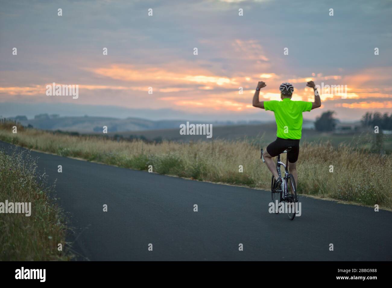 Uomo maturo che si mostra fuori mentre si guida una bicicletta lungo una strada di campagna Foto Stock