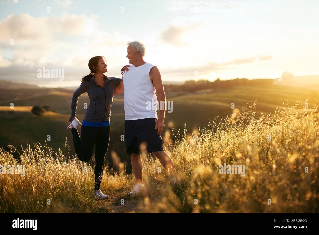 Uomo anziano e giovane donna che si allungano prima di correre su sentiero all'aperto Foto Stock