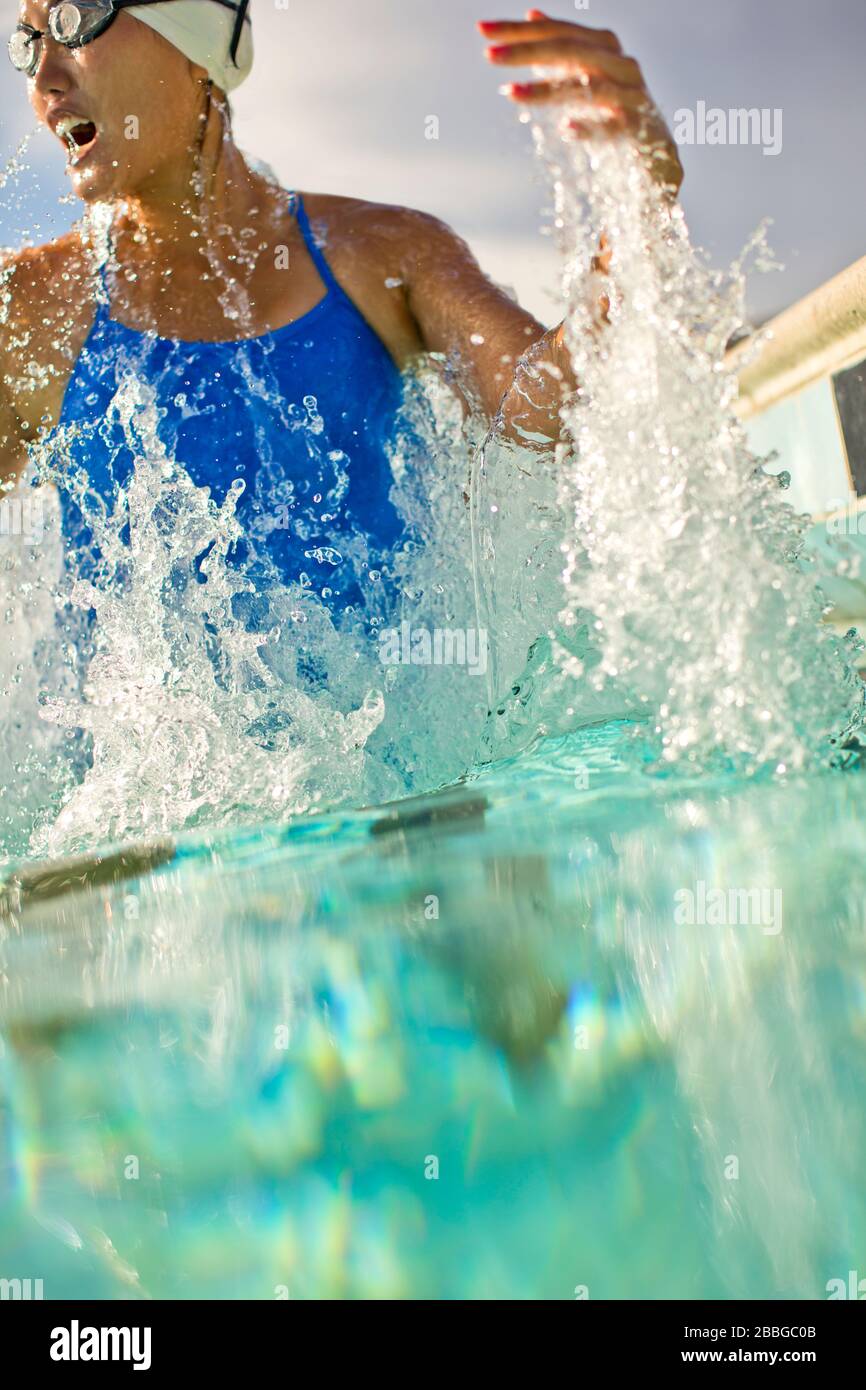 Giovane donna che salta da sotto l'acqua in una piscina Foto Stock