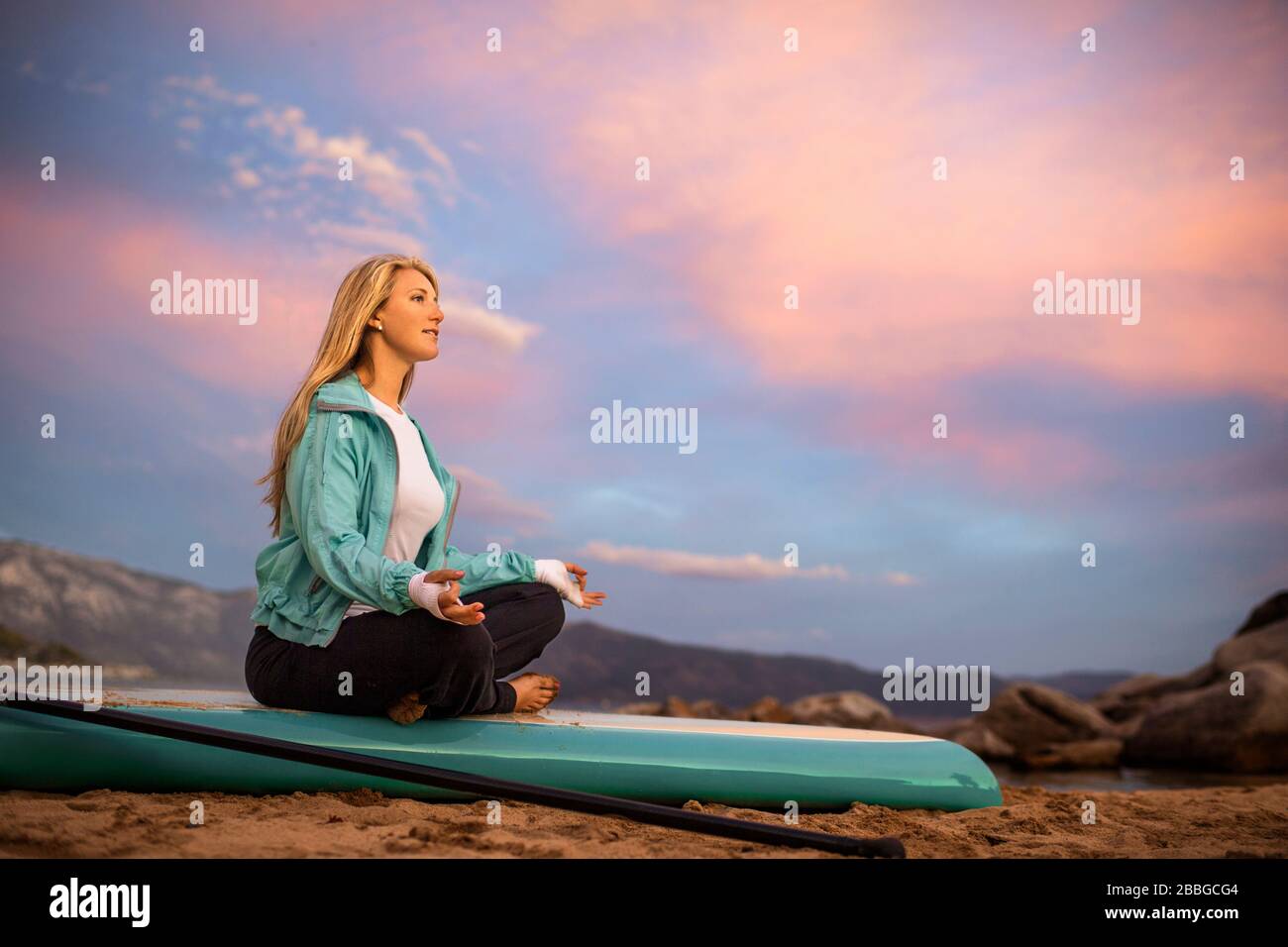 Giovane donna meditando sulla sua tavola da paddle Foto Stock