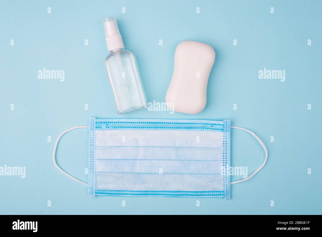 Igiene delle mani del viso. Top flatlay primo piano foto di spray antibatterico bianco sapone solido e maschera chirurgica isolato su sfondo blu Foto Stock