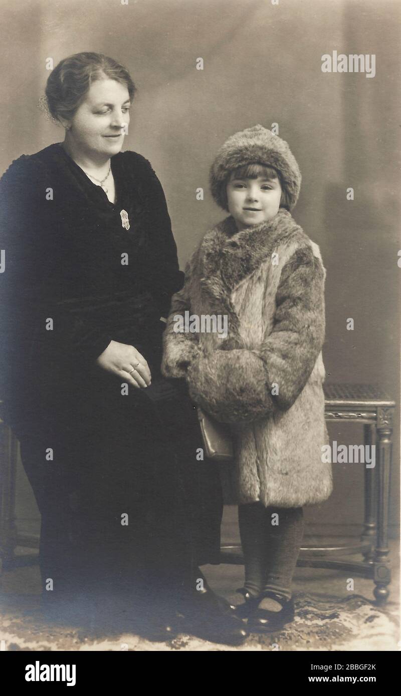 Una foto d'epoca scattata in studio intorno al 1900-19100, mostrando una giovane ragazza di 8-10 anni con la madre che posa con un abito da pelliccia reale adulto clothi Foto Stock