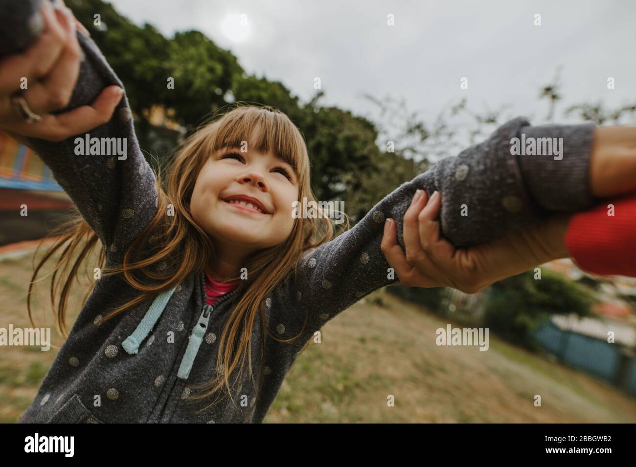 POV girato di una donna che tiene le mani di una bambina e la gira al parco. Donna che gioca con una piccola ragazza al parco giochi. Foto Stock