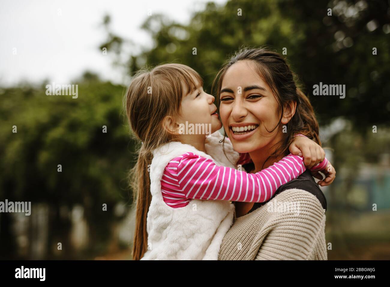 Ragazza baciare sulla guancia della sua nanny al parco. Baby sitter divertirsi con una ragazza al parco. Foto Stock