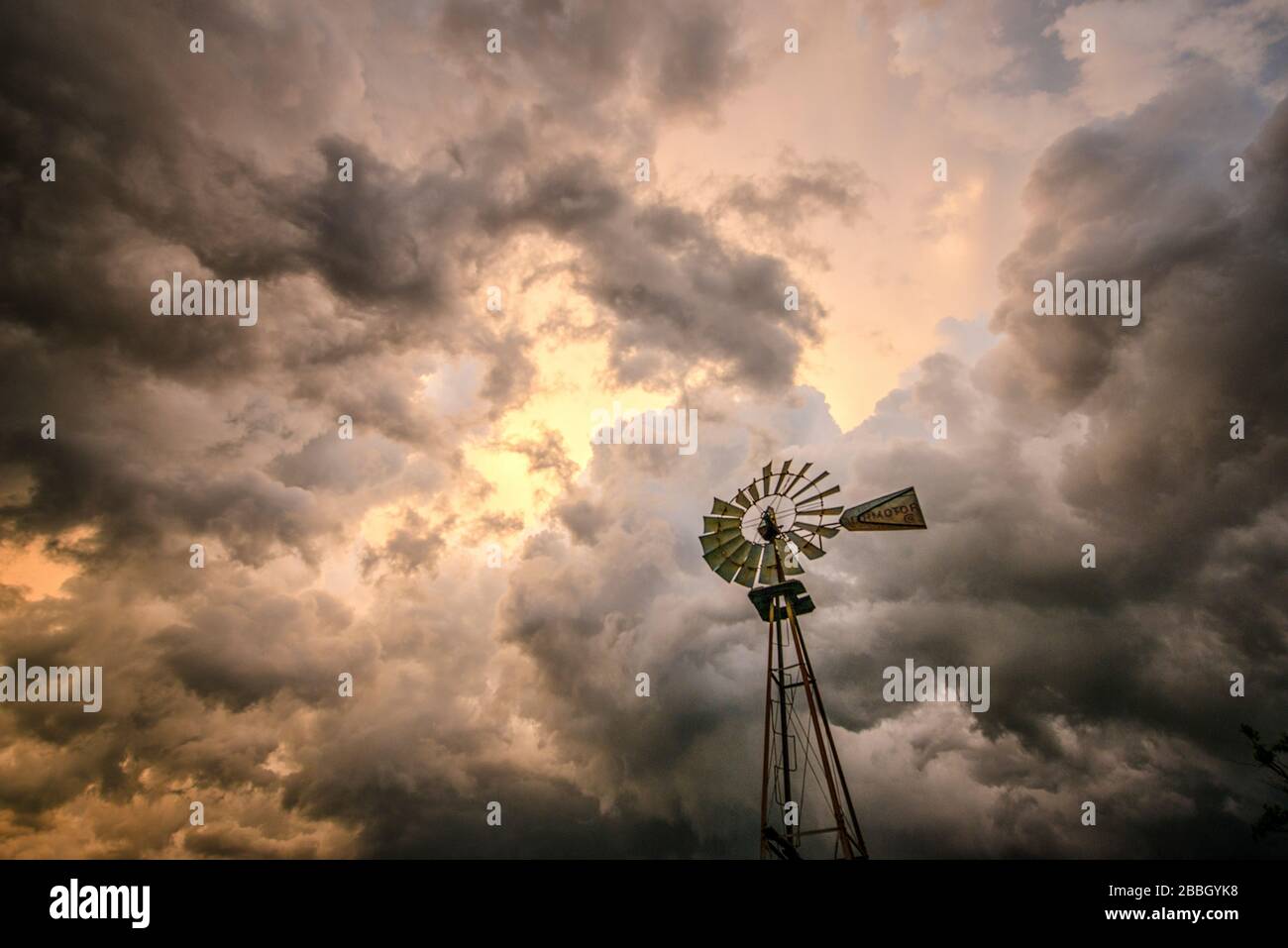 Tramonto con tempeste che rotolano sopra la testa e un mulino a vento rurale in primo piano in Kansas Stati Uniti Foto Stock