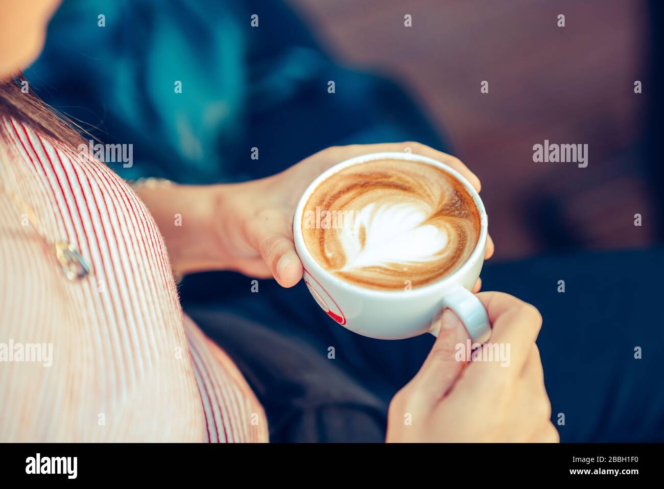 Giovane donna seduto e tenendo una tazza con caffè a forma di cuore in un caffè Foto Stock