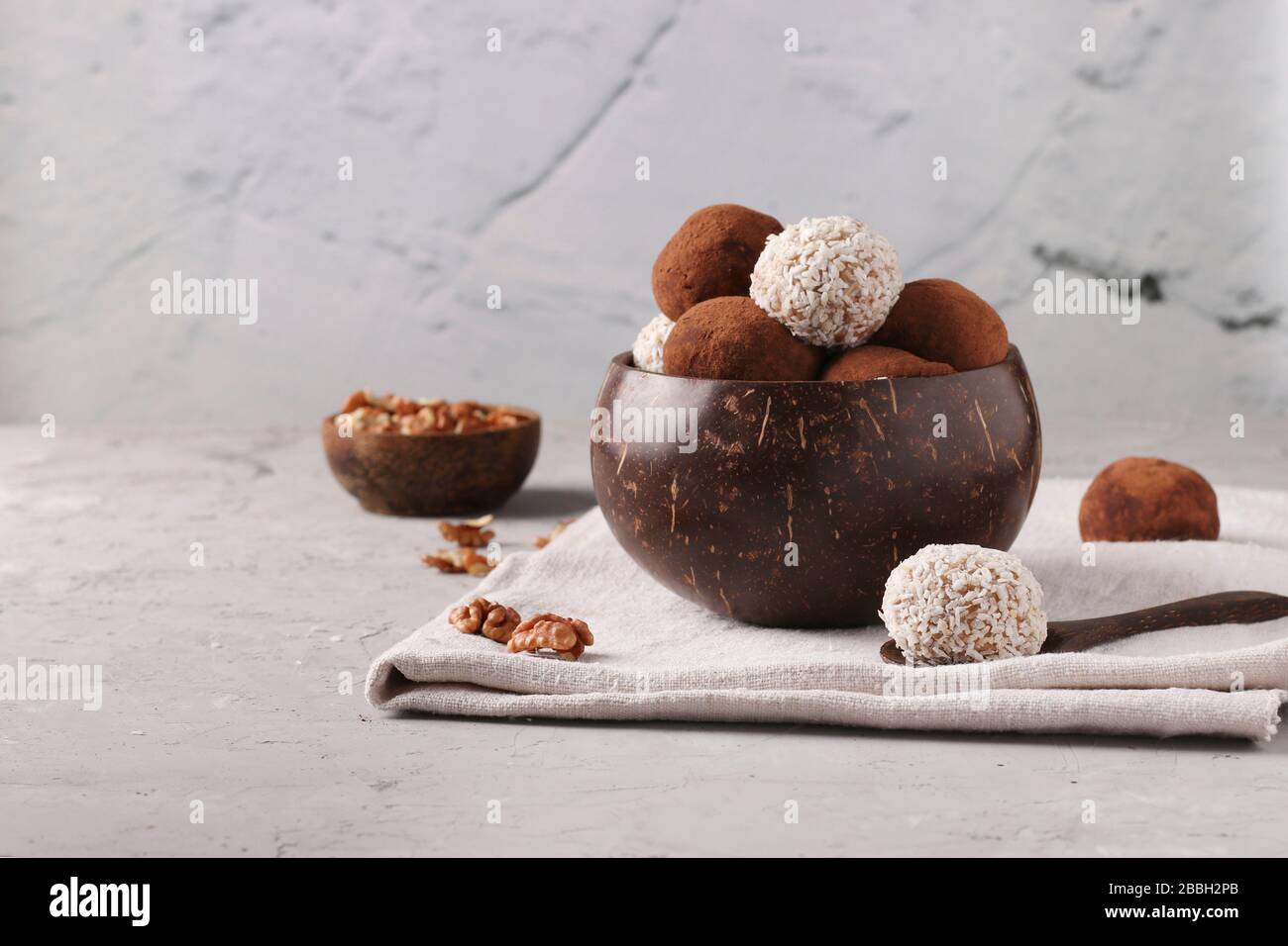 Palle di energia di noci e oatmeals con fiocchi di cocco e cacao in ciotola di cocco su sfondo grigio, formato orizzontale Foto Stock