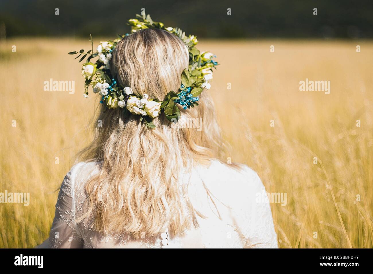 Retro della giovane donna in un abito bianco in stile boho con una corona floreale in estate nel campo. Foto Stock
