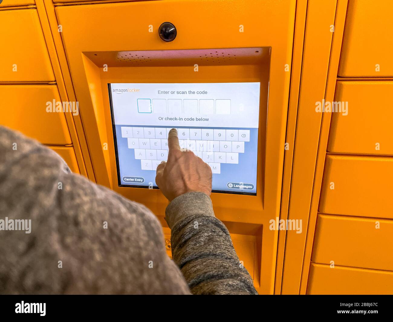 Uomo che utilizza Amazon Locker nel centro commerciale, punto di prelievo arancione per gli ordini di posta con il logo del marchio Amazon su di esso. Fotografia mobile. Lione, Francia - F. Foto Stock