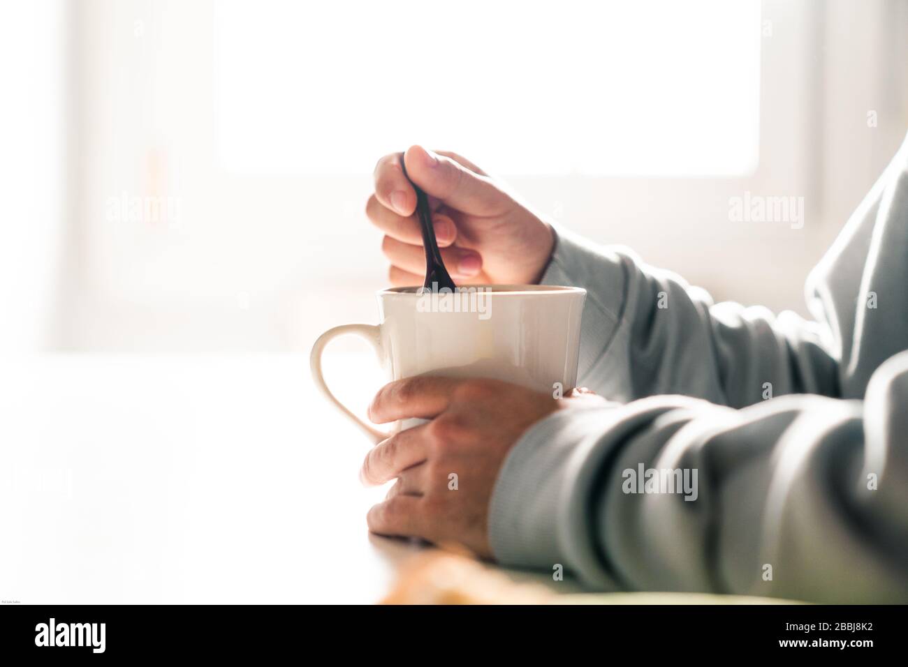 Persona che agita una tazza di caffè con un cucchiaio di ceramica. Le mani di una persona. Foto Stock