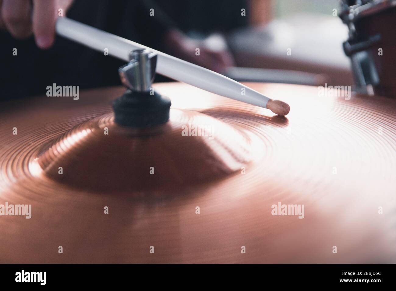 Primo piano della mano di un batterista che tiene i bastoni bianchi del tamburo mentre si siede dietro un set del tamburo. Foto Stock