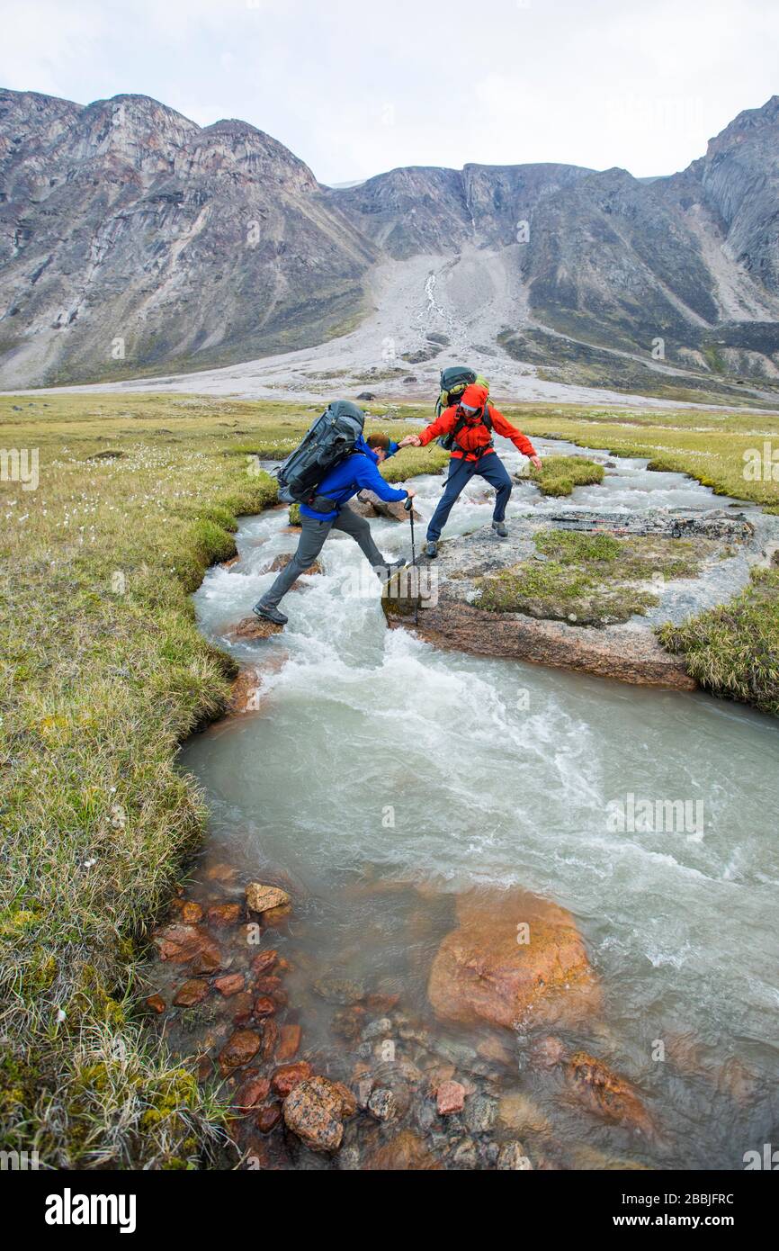 Backpackers aiutarsi l'un l'altro attraversare un fiume in Akshayak Pass. Foto Stock