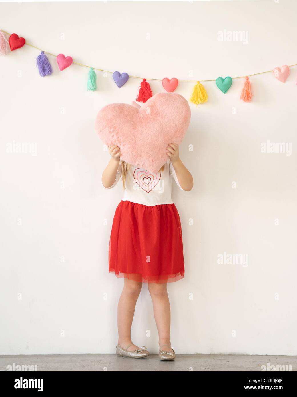bambina in rosso tutu tenendo il cuscino cuore peluche rosa sulla faccia Foto Stock
