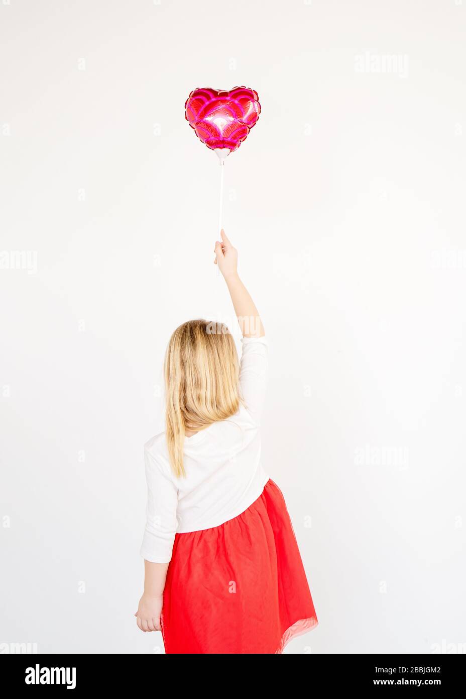 indietro vista piccola bionda ragazza in rosso tutu tenendo rosso cuore palloncino Foto Stock