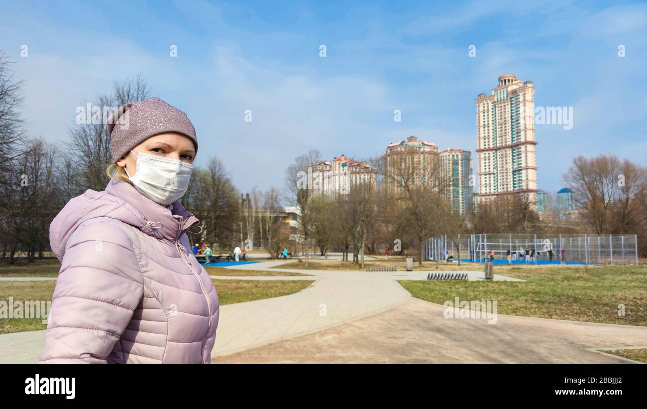 Donna con maschera chirurgica sul viso nel parco cittadino durante la pandemia di coronavirus COVID-19. Persone che indossano maschera medica per strada a causa della malattia di coronavirus. Foto Stock