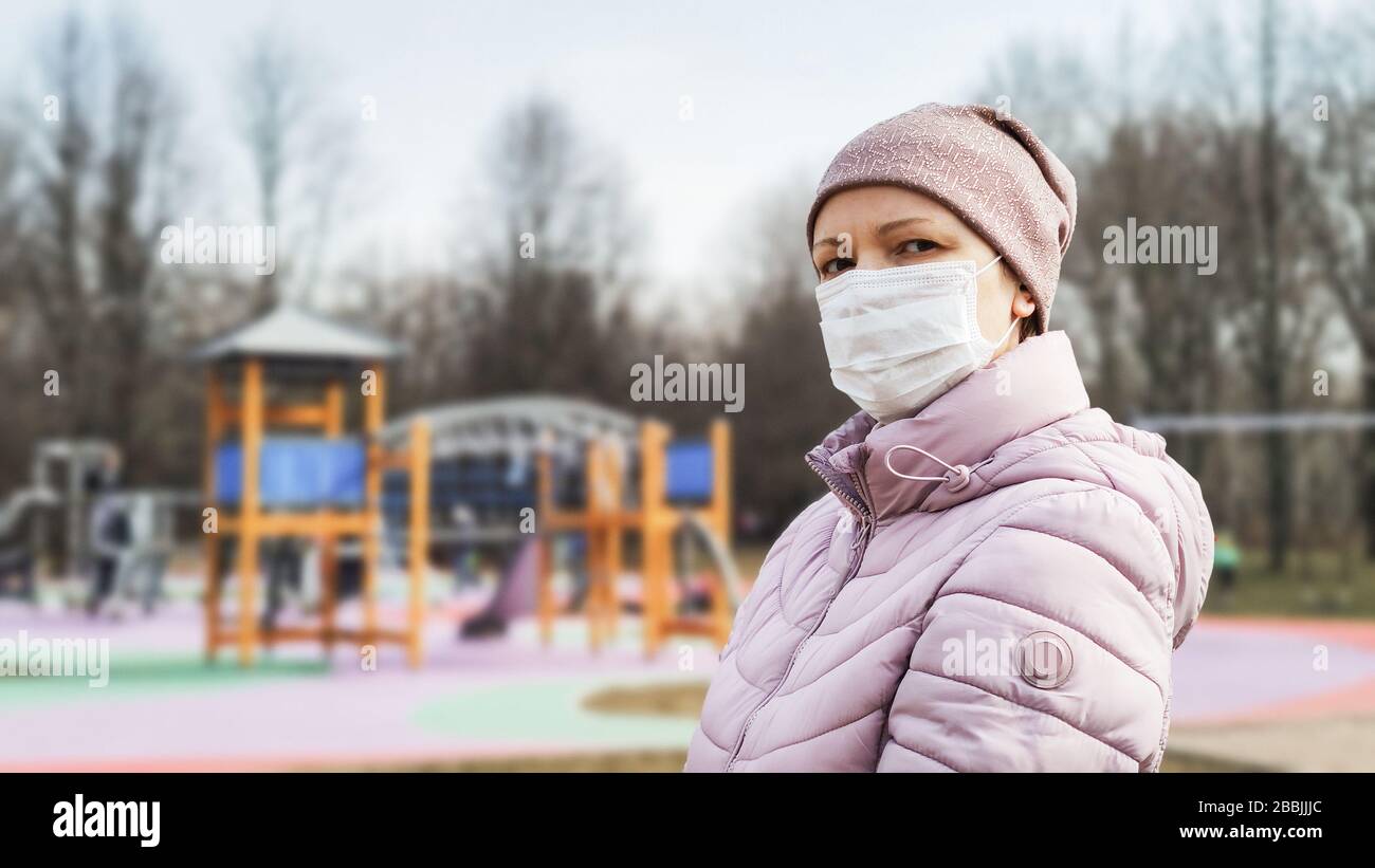 Donna al parco giochi con maschera chirurgica sul viso durante la pandemia di coronavirus COVID-19. Persone che indossano maschera medica per strada a causa della malattia di coronavirus. Foto Stock