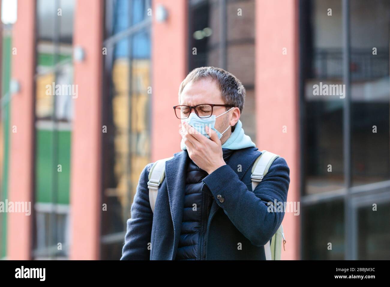L'uomo negli occhiali si sente ammalato all'aperto, tossendo, indossando la maschera protettiva contro le malattie infettive trasmissibili, allergia al polline, protezione contro Foto Stock