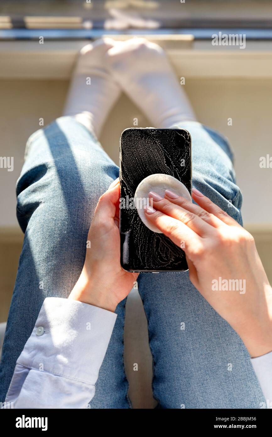 Donna pulizia cellulare per eliminare germi, coronavirus, covid-19, batterie. La femmina disinfetta uno smartphone applicando disinfettante/disinfettante con alcol Foto Stock