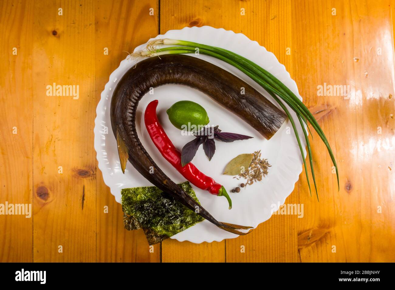 Garfish affumicato con lime, basilico, cipolle verdi, peperoncino, patatine, spezie, olio di oliva in un piatto bianco di ceramica, su un tavolo di legno Foto Stock