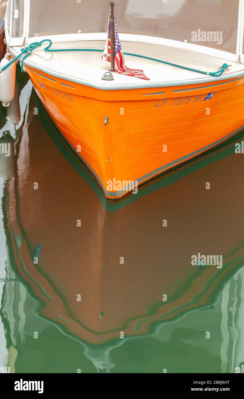 Testa di una barca di colore arancione con bandiera americana e si riflette sull'acqua. Foto Stock