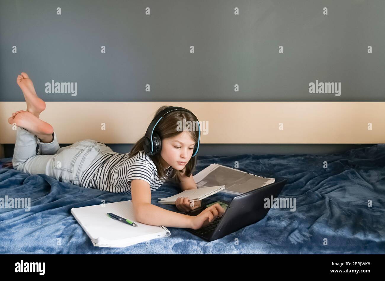 Il concetto di autoisolamento online per l'apprendimento a distanza. La bambina seduto a casa fa i compiti attraverso il portatile digitale Foto Stock