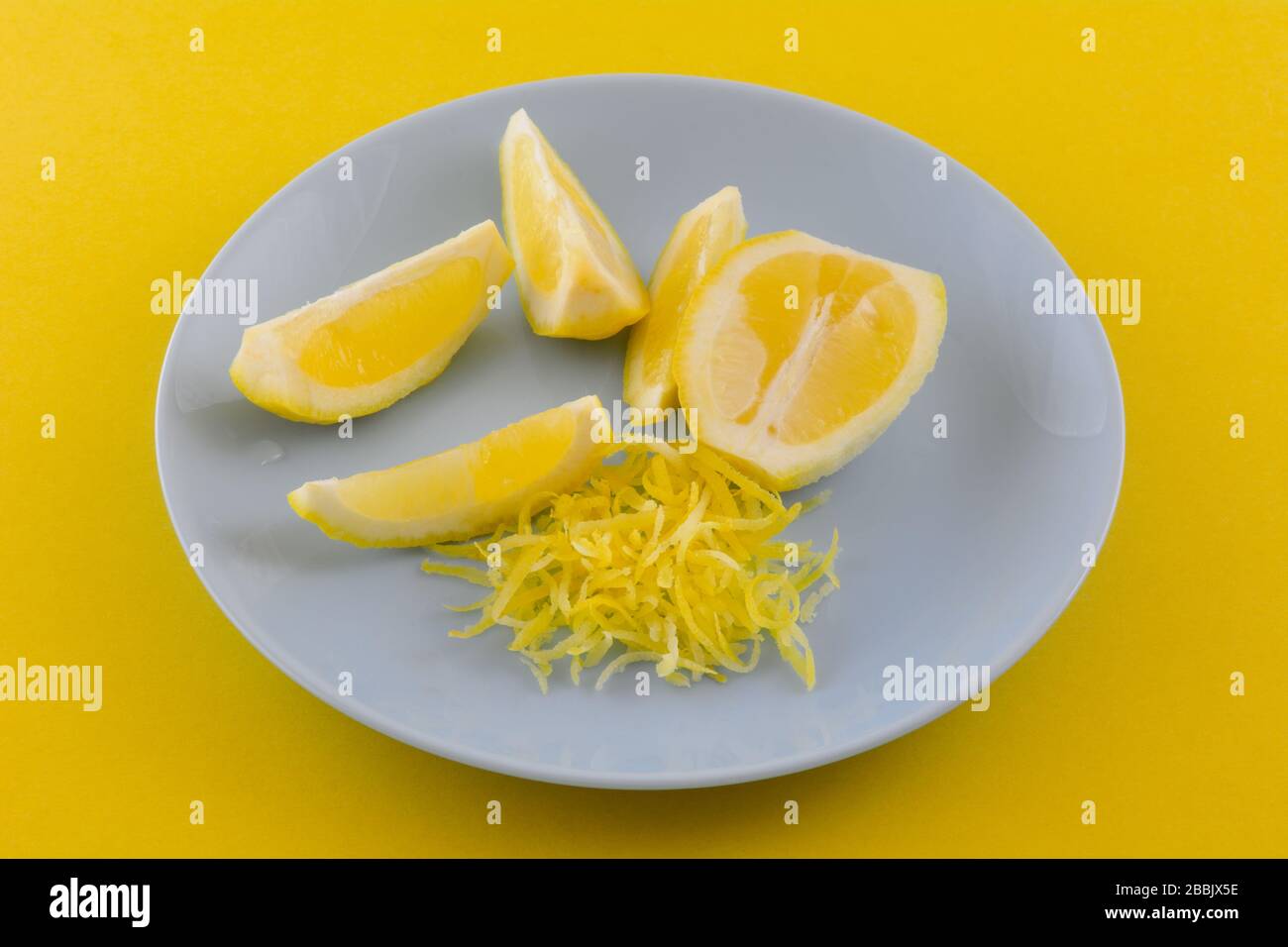Mezzo limone, spicchi di limone e scorza di limone su piastra blu su sfondo giallo Foto Stock