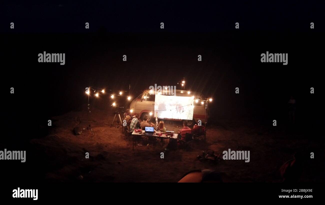 Amici che guardano il film sullo schermo in Campsite Foto Stock