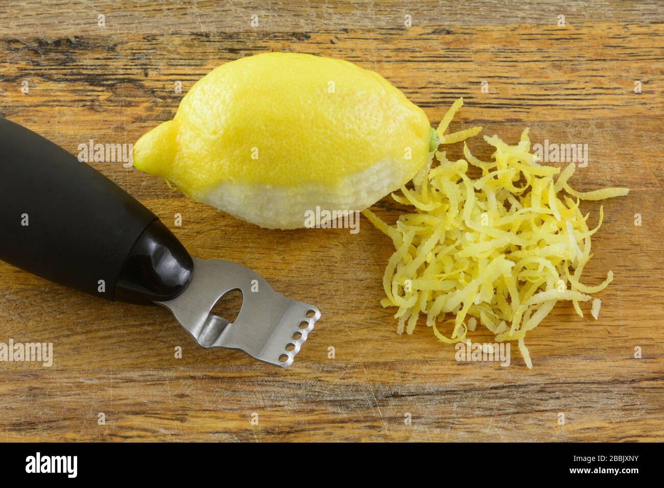 Limone con pelo di scorza di limone e zester su tagliere di legno Foto Stock