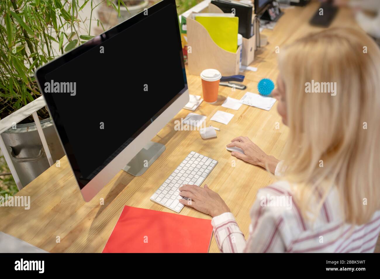 Donna bionda seduta alla scrivania, al lavoro al computer Foto Stock