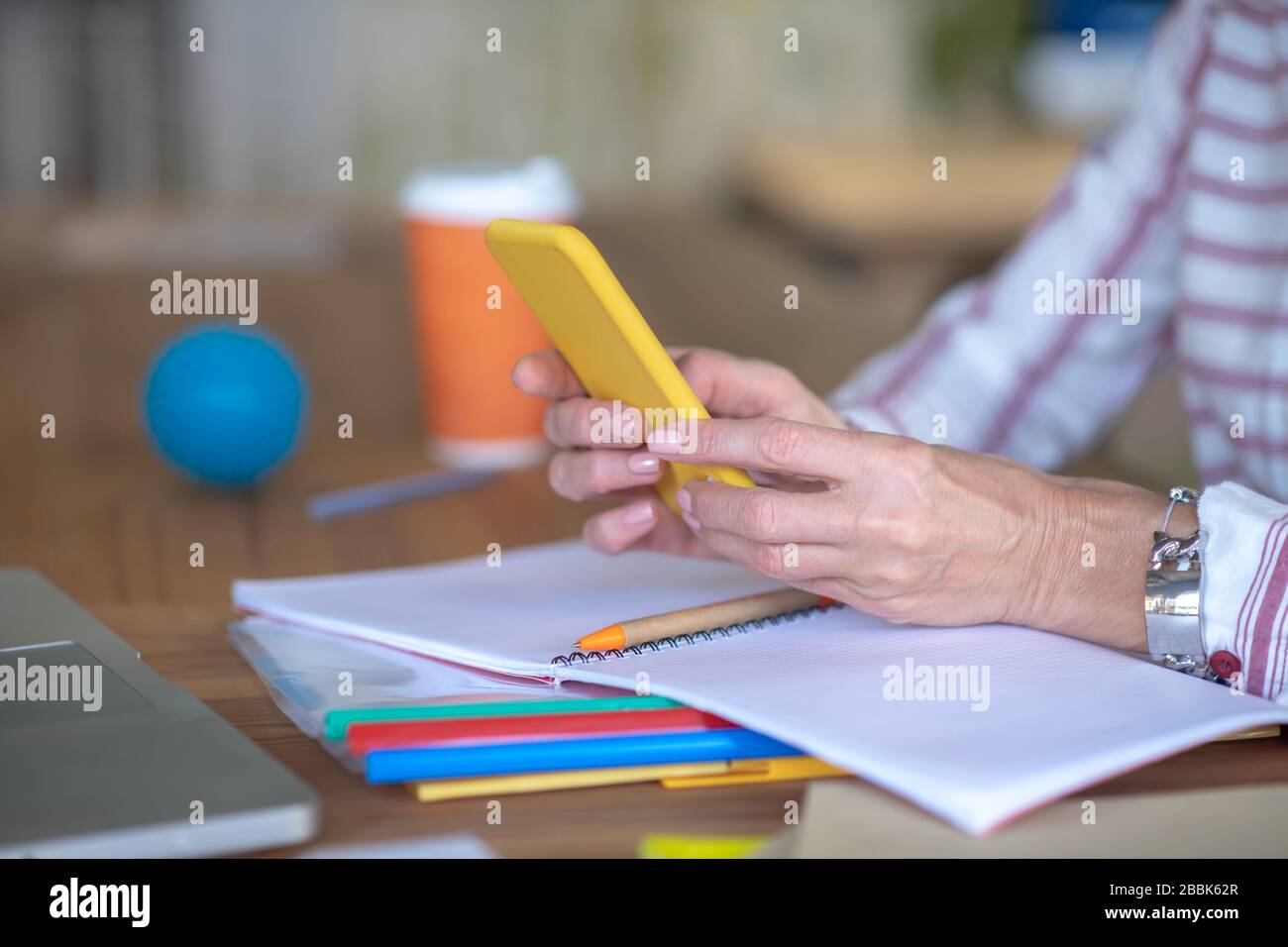 Le mani femminili tengono il telefono cellulare giallo sopra il notebook Foto Stock