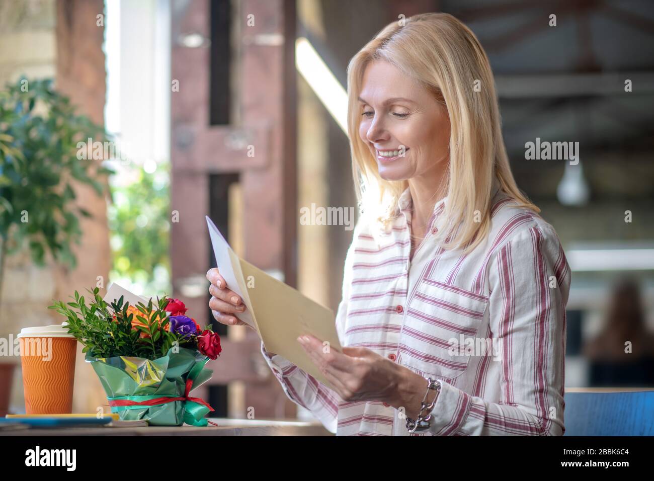 Felice bionda donna ha ricevuto lettera e fiori, sorridendo Foto Stock