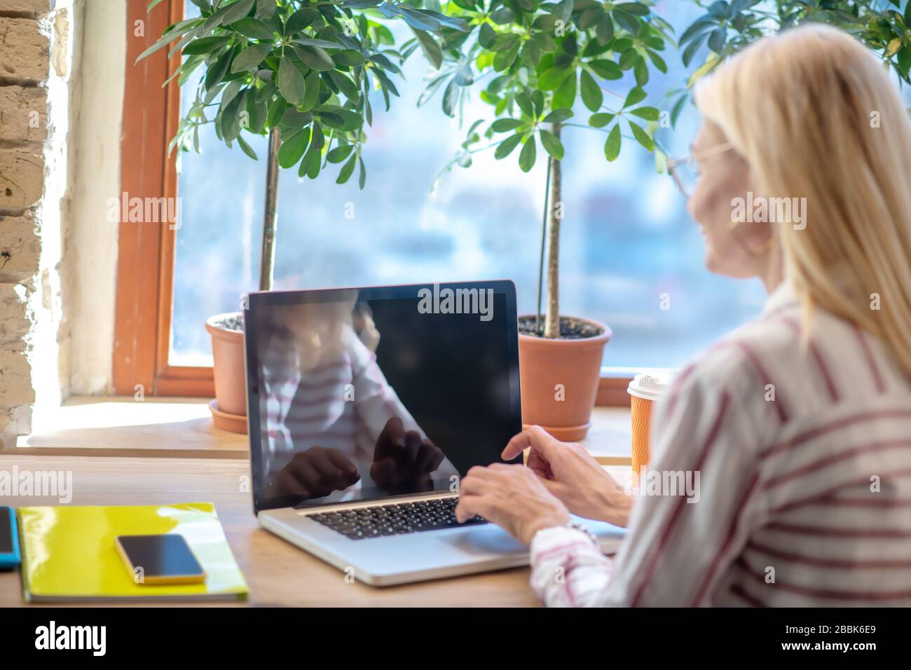Donna bionda seduto alla scrivania, digitando sul computer portatile, torna alla fotocamera Foto Stock