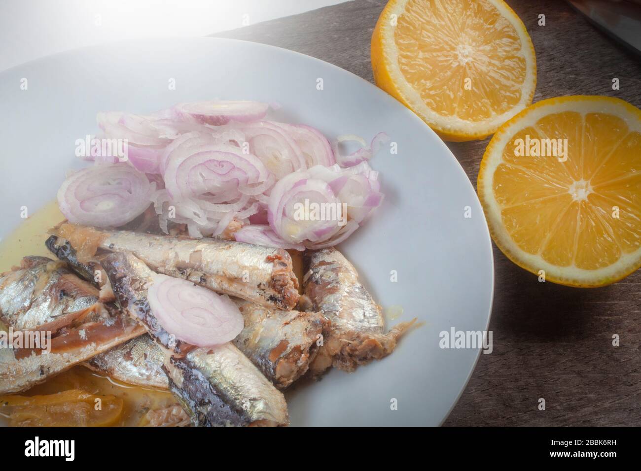 studio foto di sardinas con due limoni tagliati su una lastra bianca dalla composizione superiore su sfondo di legno Foto Stock