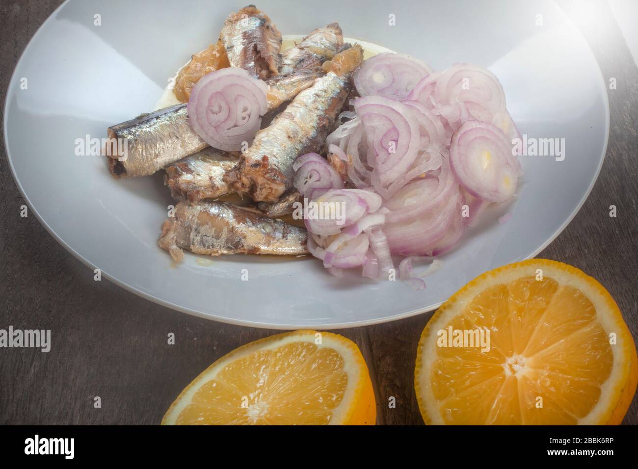 studio foto di sardinas con due limoni tagliati su una lastra bianca dalla composizione superiore su sfondo di legno Foto Stock